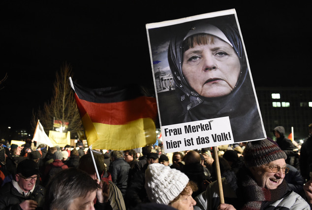 A protestor holds a poster with a picture of German Chancellor Angela Merkel reading 'Mrs Merkel, her is the people' during a rally of the group Patriotic Europeans against the Islamization of the West, or PEGIDA, in Dresden, Germany, Monday, Jan. 12, 2015. (AP Photo/Jens Meyer)