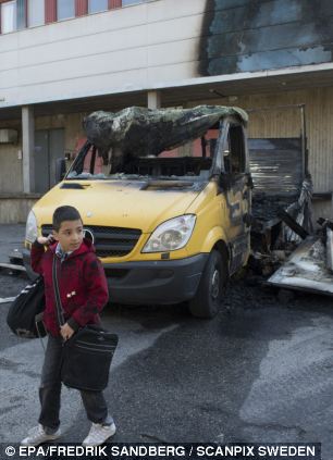 A boy walks to school past a burned out truck outside a scorched building