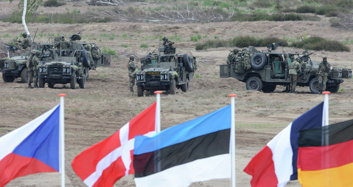 Flags wave in front of soldiers who take positions with their army vehicles during the NATO Noble Jump exercise on a training range near Swietoszow Zagan, Poland, Thursday, June 18, 2015.