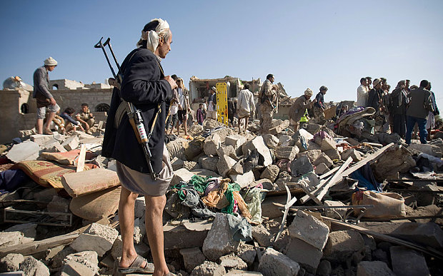 A Houthi Shiite fighter stands guard as people search for survivors under the rubble of houses destroyed by Saudi airstrikes near Sanaa Airport 