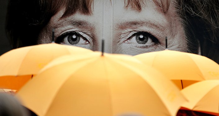 Supporters of the Christian Democratic Union (CDU) hold umbrellas in front of a giant portrait of German Chancellor Angela Merkel during an election campaign event in front of the party's headquarter in Berlin, Germany, Monday, Sept. 16, 2013.