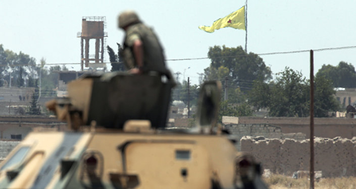 In this photo taken from the Turkish side of the border between Turkey and Syria, in Akcakale, southeastern Turkey, a Turkish soldier on an armoured personnel carrier watches as in the background a flag of the Kurdish People's Protection Units, or YPG, is raised over the city of Tal Abyad, Syria, Tuesday, June 16, 2015
