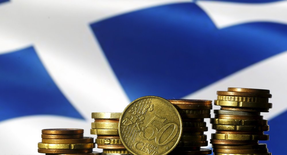 Euro coins are seen in front of a displayed Greece flag