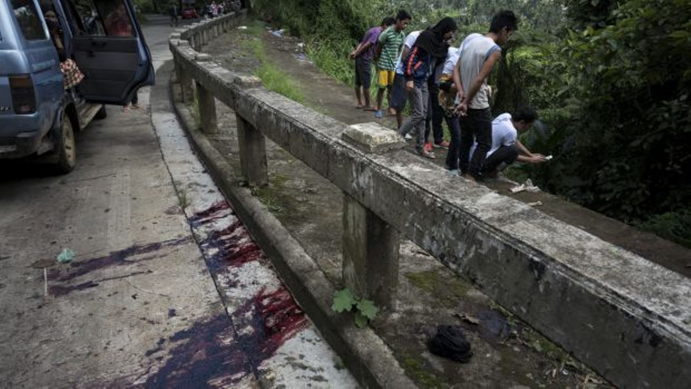 Blood stains the roadside as civilians view unidentified bodies believed to have been executed and dumped in a ditch by militants